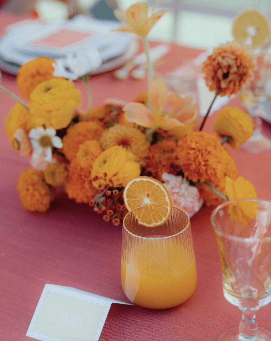 Bloom forward centerpiece featuring dahlias and marigolds with an orange cocktail for a fall welcome brunch